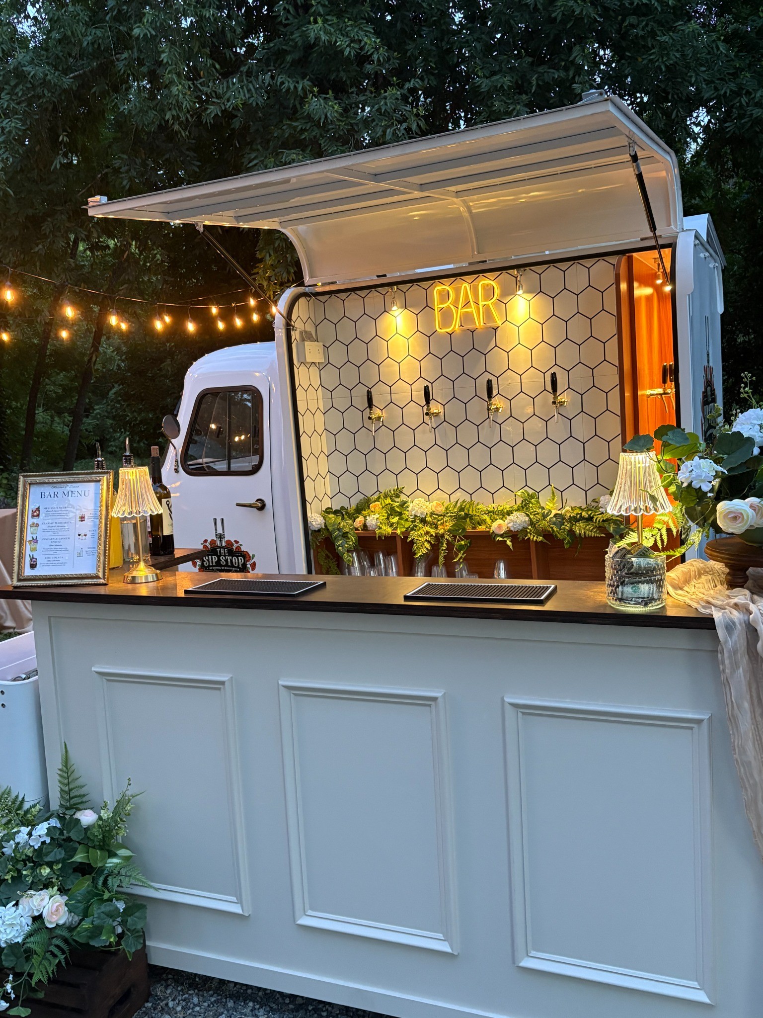 White Piaggio and portable bar with flowers and glowing lamps at an evening celebration