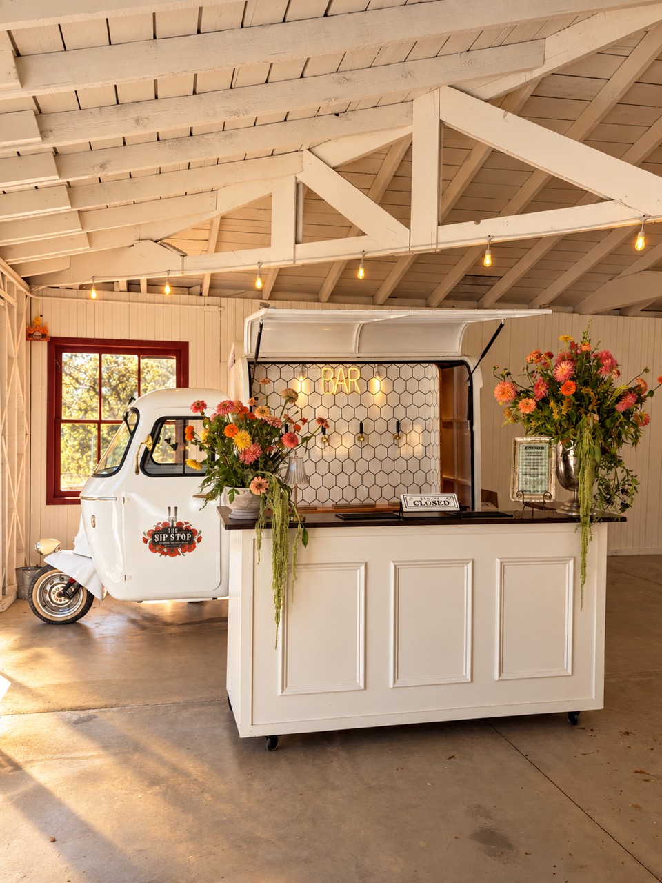 White Piaggio and portable bar with flowers inside a white-beamed venue