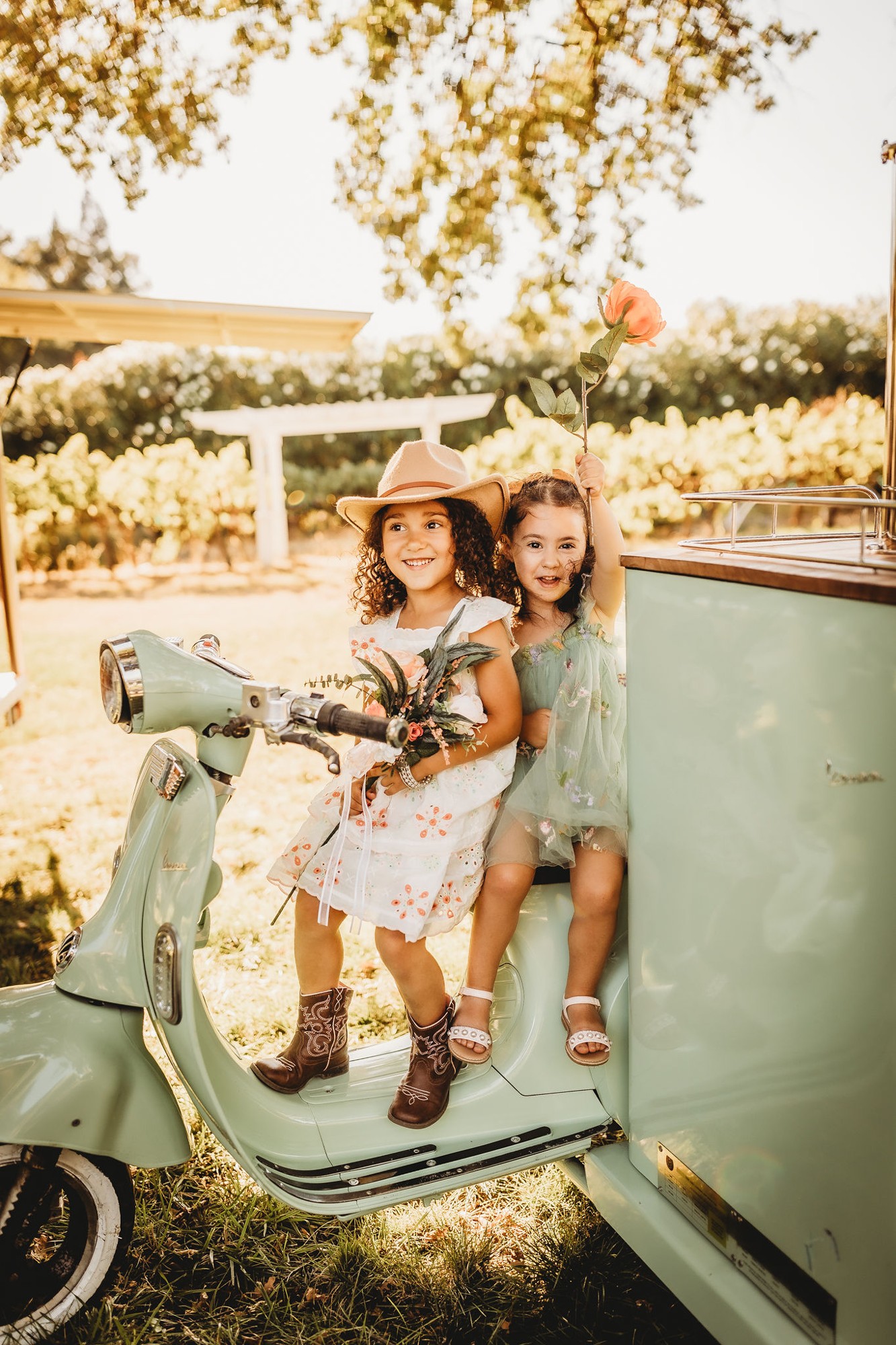 Two children seated on the mint-green Vespa tap cart at an outdoor celebration